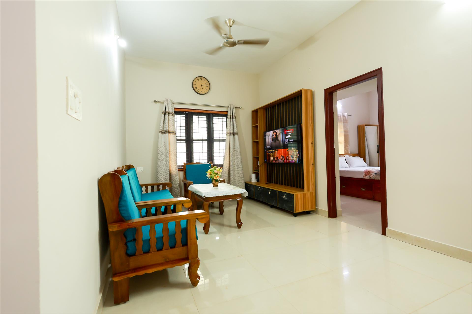 Living area with TV unit, teak chairs, and bedroom view beyond